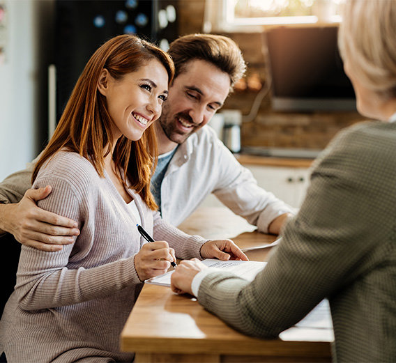 Couple smiling at mortgage broker while signing a paper.